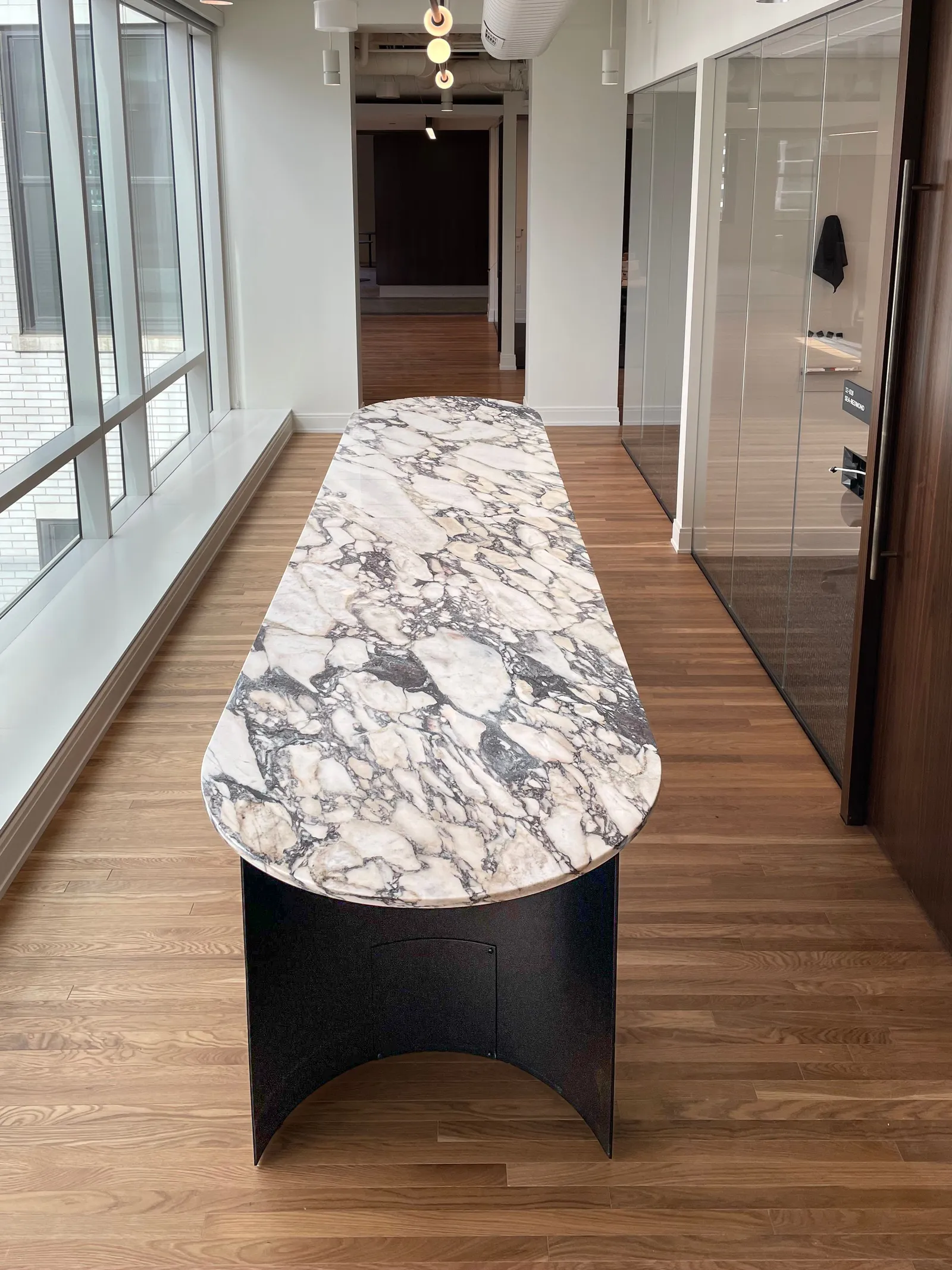custom pill-shaped stone table with creacent-shaped steel base by Icon Modern